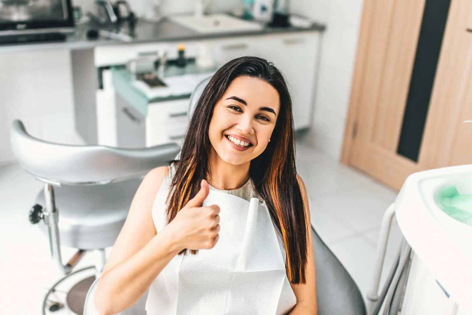 Smiling woman sitting in dental chair giving thumbs up in a dental clinic.