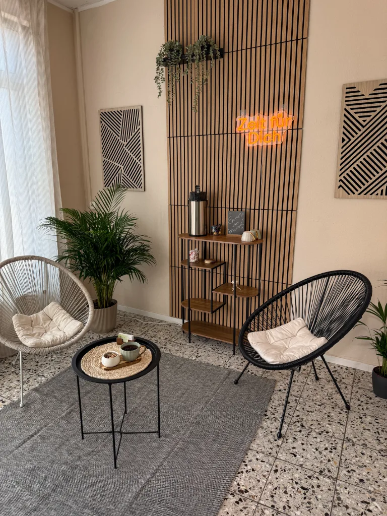 Empfangsbereich im Massagestudio Kassel mit gemütlichen Stühlen, Pflanzen und dem Neonschriftzug „Zeit für Dich"