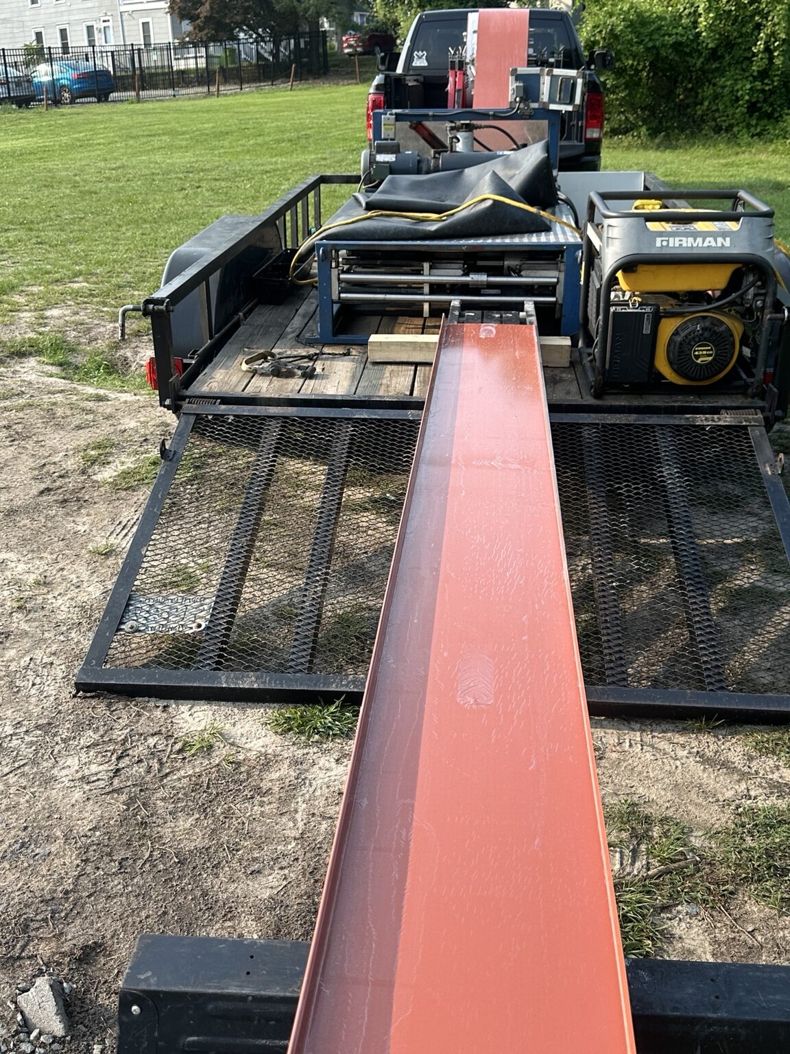 Long red metal wall panel extending from portable roll-forming equipment at a jobsite