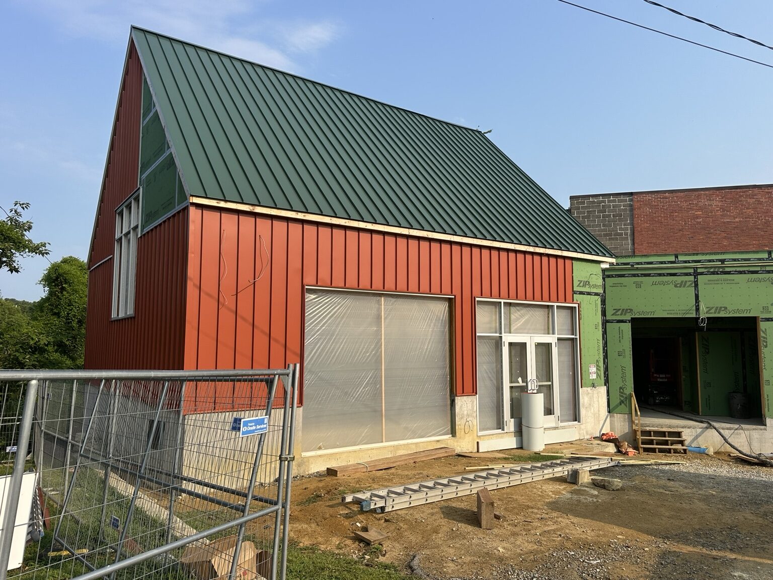 Wide view of red vertical metal wall panels beneath a green standing-seam roof on a building under construction