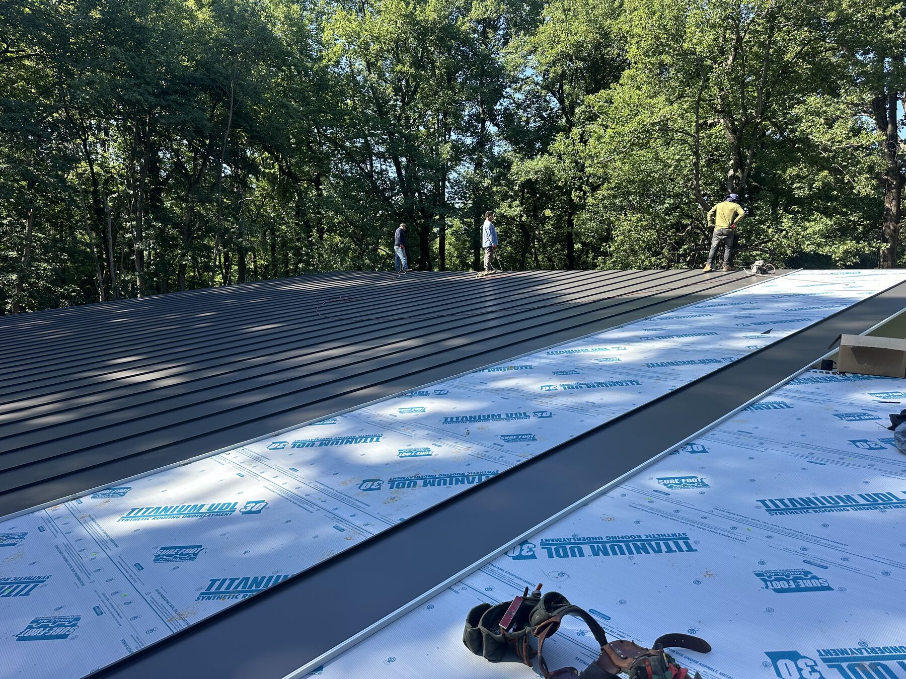 Dark standing-seam roofing panels being installed during active construction
