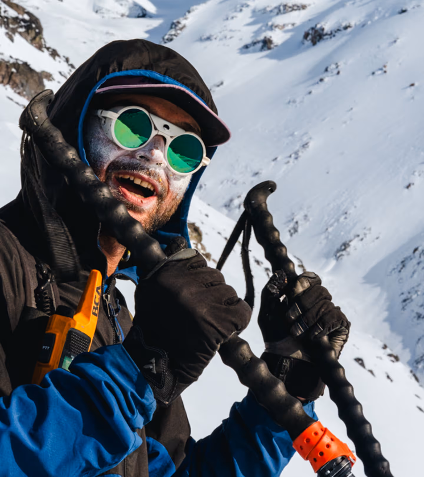 Stratton Matteson with white face sunscreen, sunglasses, and gloves holding ski poles in snowy mountain.