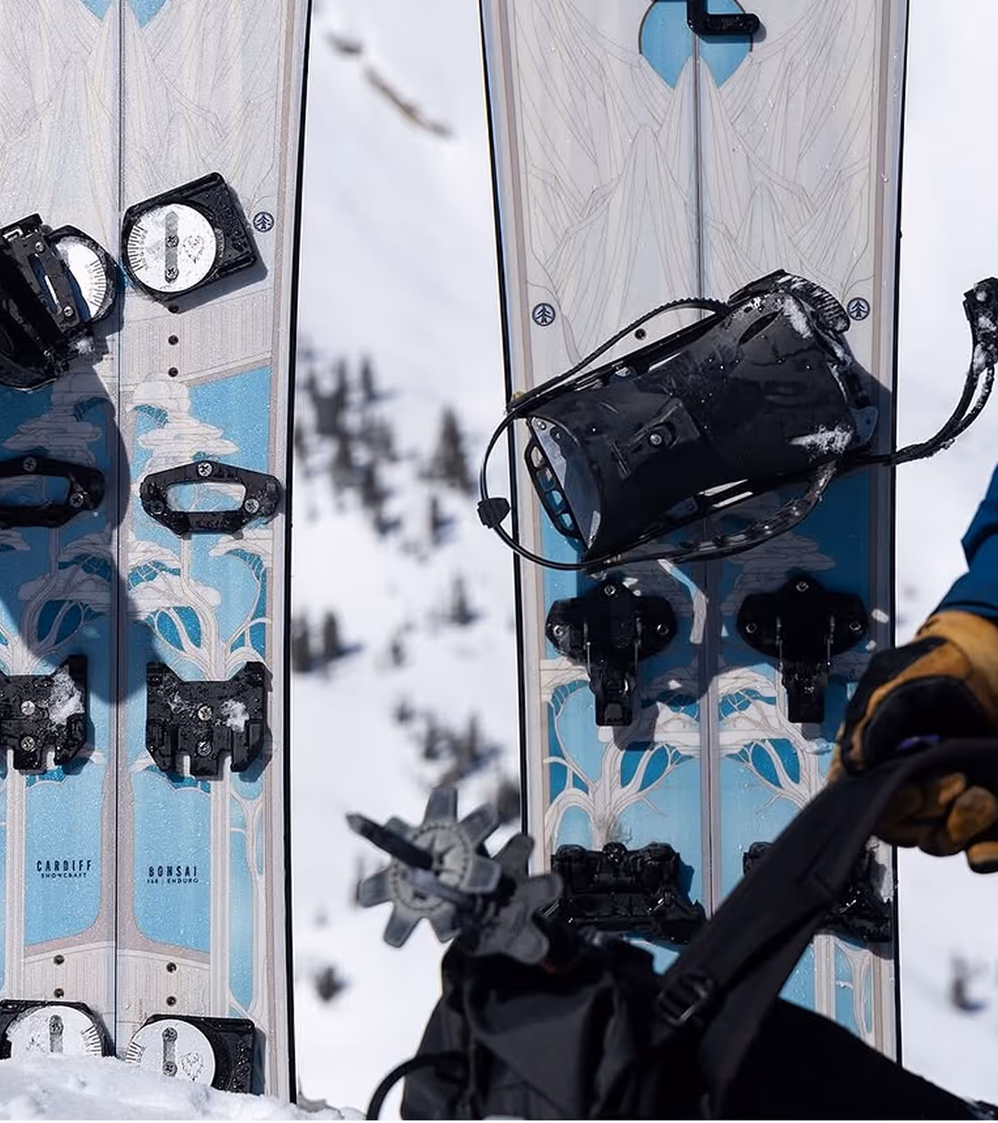 Pair of Cardiff Bonsai skis with bindings on snow, with gloved hand holding ski poles.