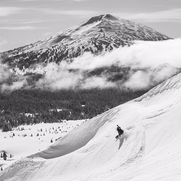Stratton carving down a steep powder run below a cloud-wrapped mountain peak.