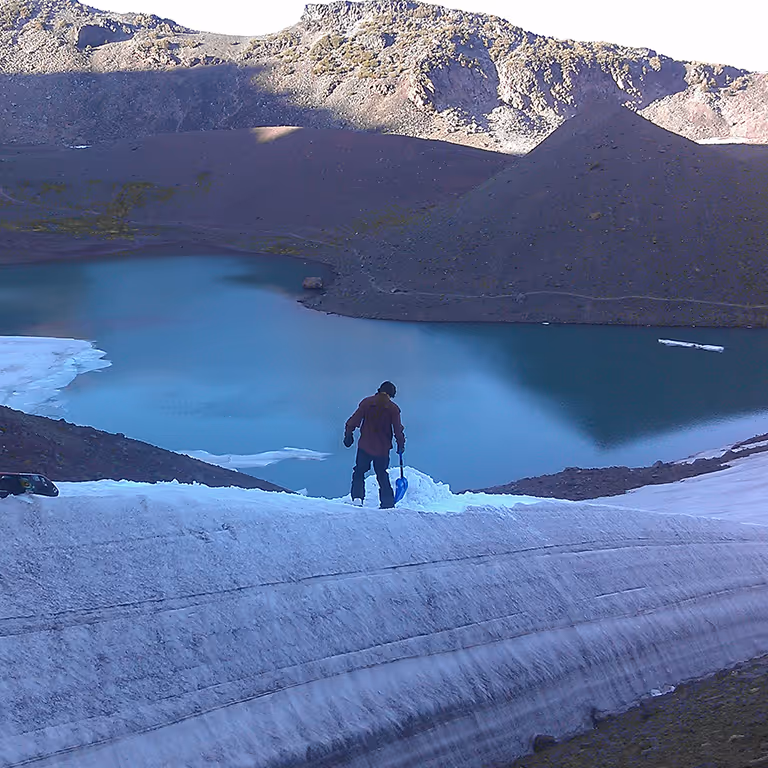 Stratton splitboarding alone on a snow-covered ridge above a turquoise mountain lake.