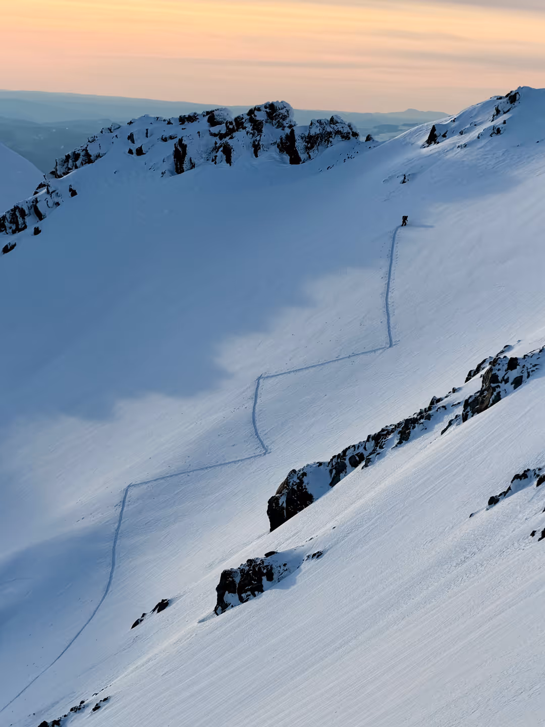 Stratton's split board tracks trailing down a vast snow-covered mountain slope at sunset