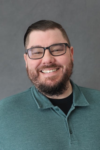 Micah Moffett, Technical Advisor at PixelPath Advisory, smiling in a teal polo shirt against a gray studio background.
