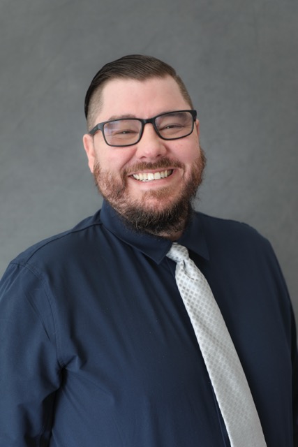 Micah Moffett, Technical Advisor at PixelPath Advisory, smiling in a navy button-down shirt and light gray tie against a gray studio background.