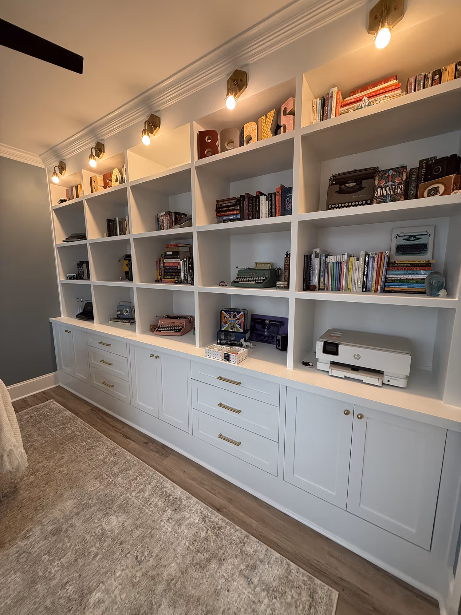 White built-in shelves with vintage typewriters, books, and decor under warm ceiling lights.