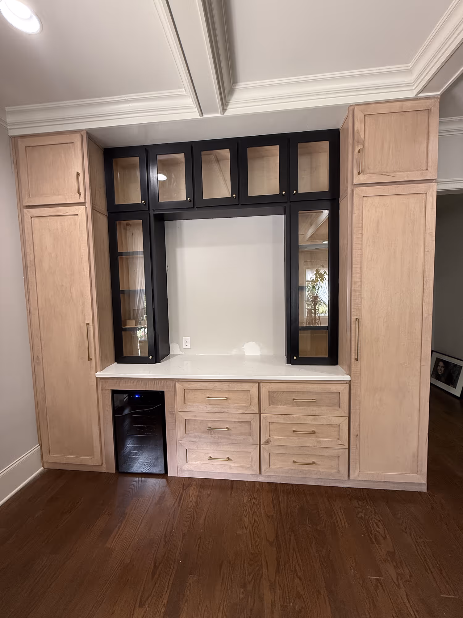 Built-in wood cabinetry with black glass doors, six drawers, and a small black fridge on dark hardwood floor.