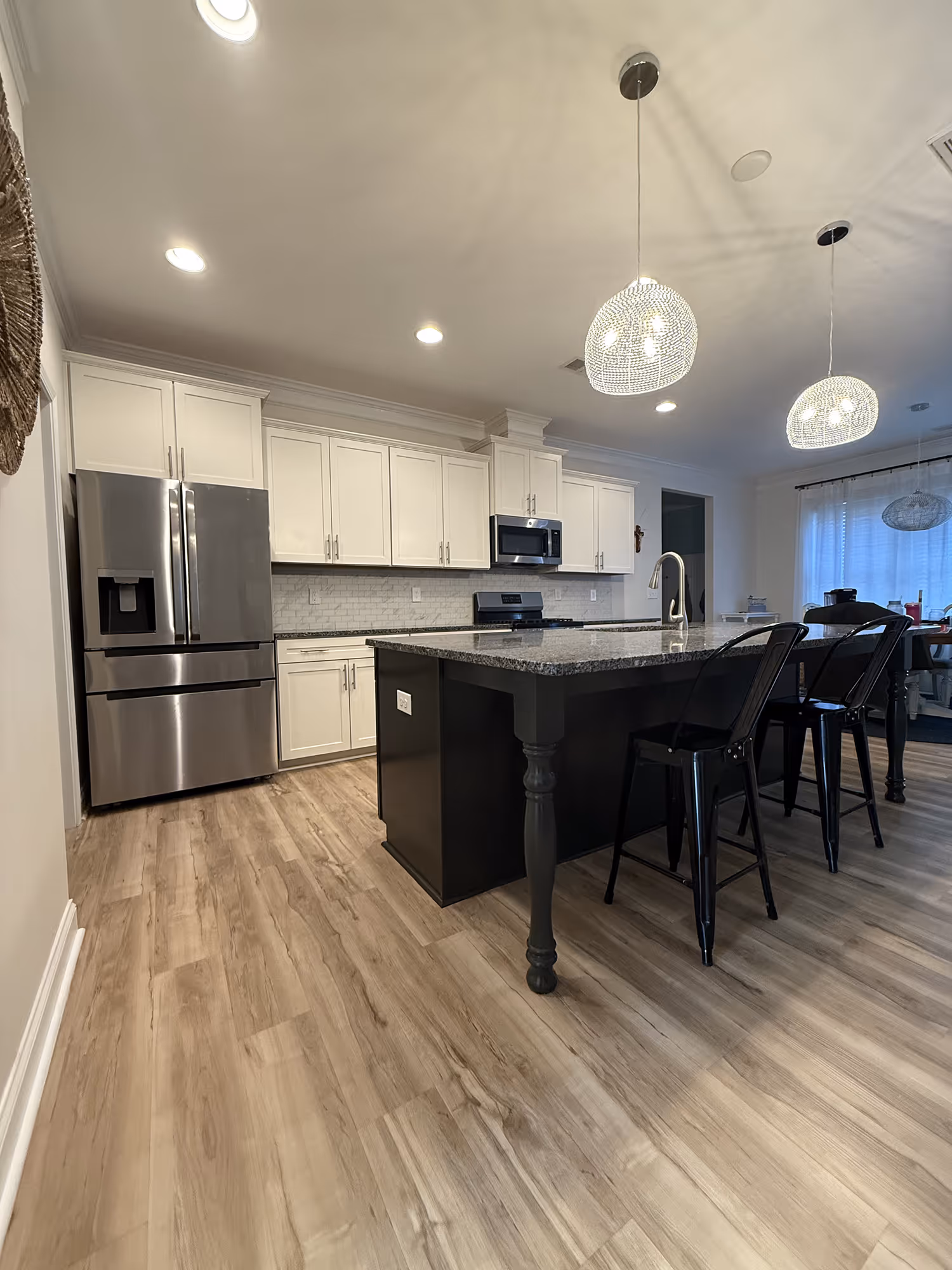 Modern kitchen with stainless steel fridge, white cabinets, black island, and wood-look flooring.