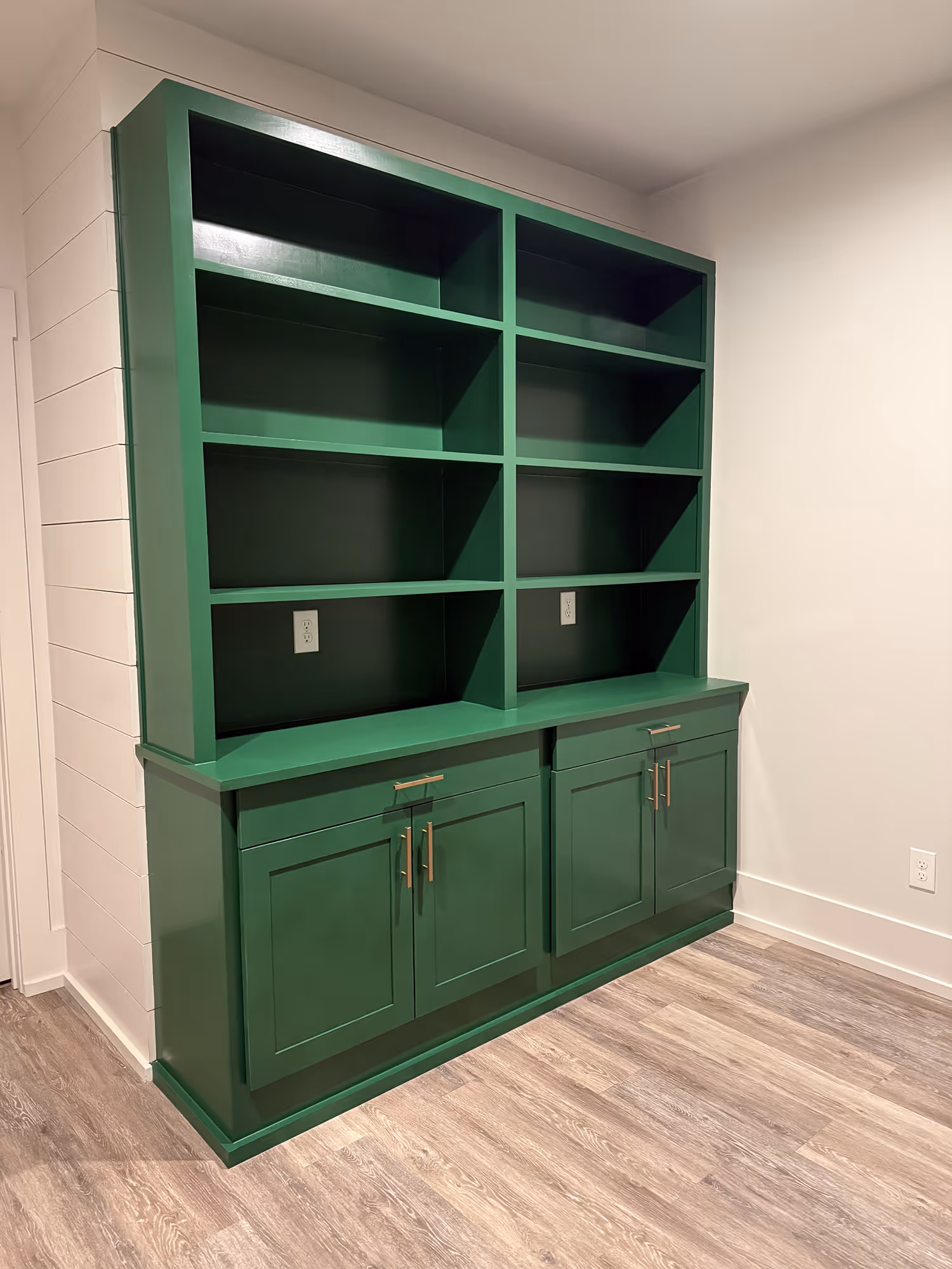 Green built-in shelves with cabinets below on wood floor against white walls.