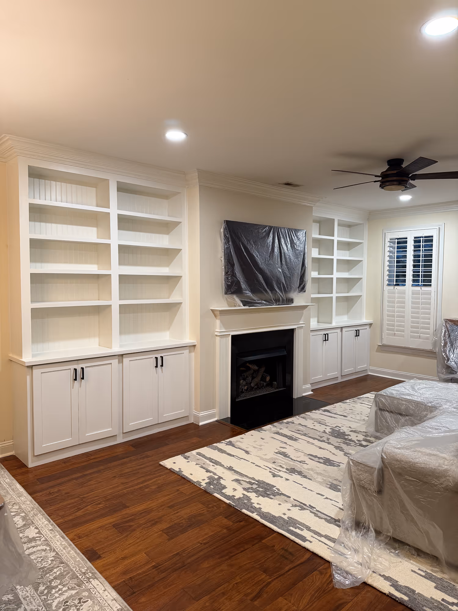Living room with white built-in shelves, a fireplace, covered TV and furniture wrapped in plastic.
