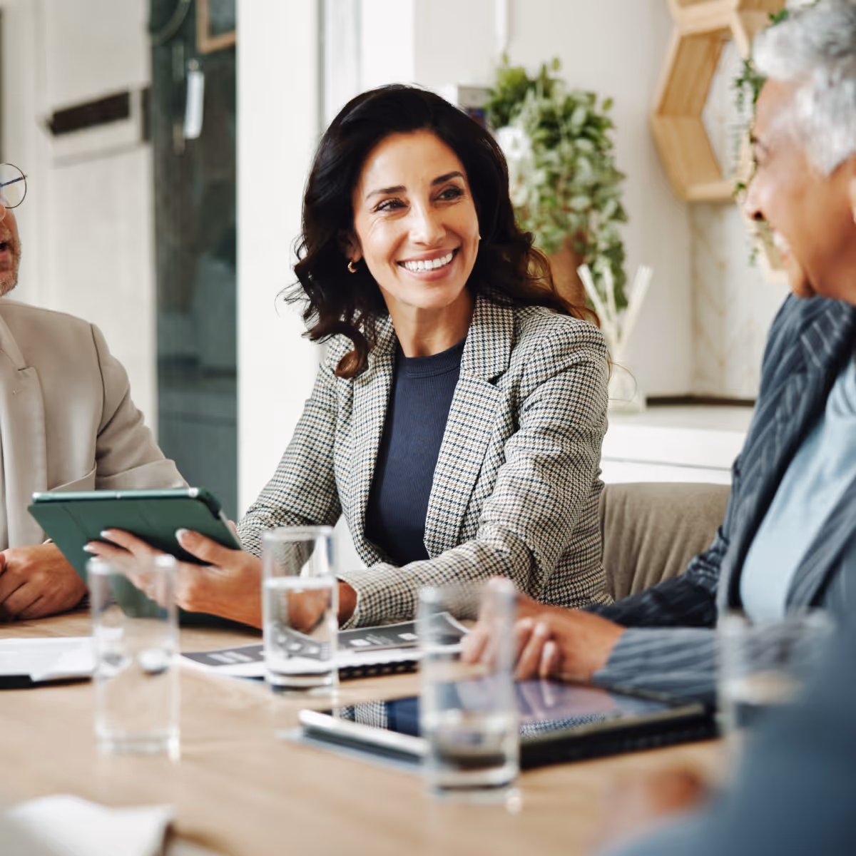 Businesswoman holding tablet in a meeting with colleagues around a table.
