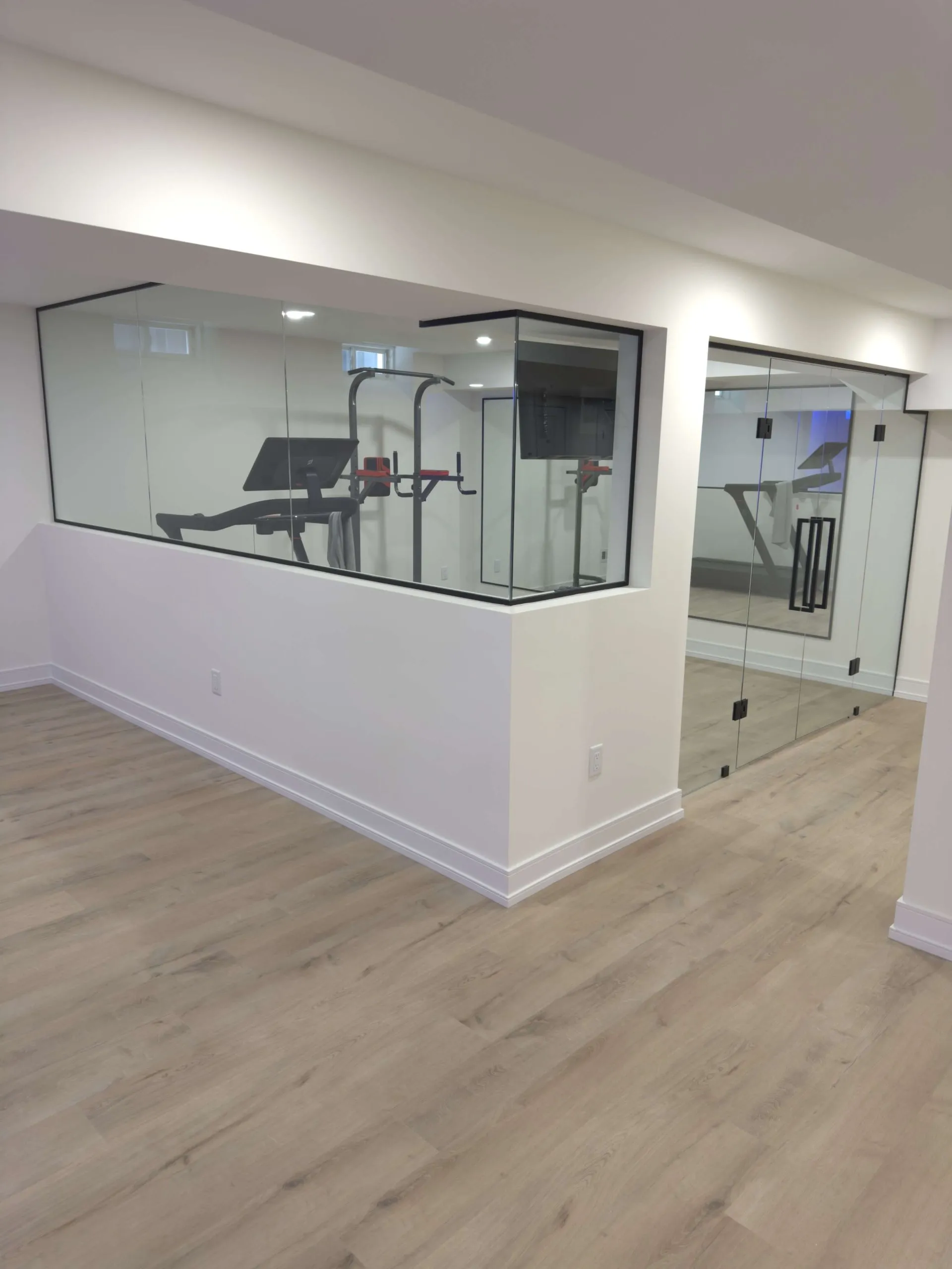 Glass walled basement gym with mirrored walls and light wood floors in a finished GTA basement by Desire Basements