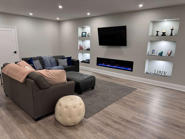 A Basement Living room showcasing the Basement Renovation Finishes with a focus on custom fireplace, custom wall niches, TV mount, and custom hardwood flooring