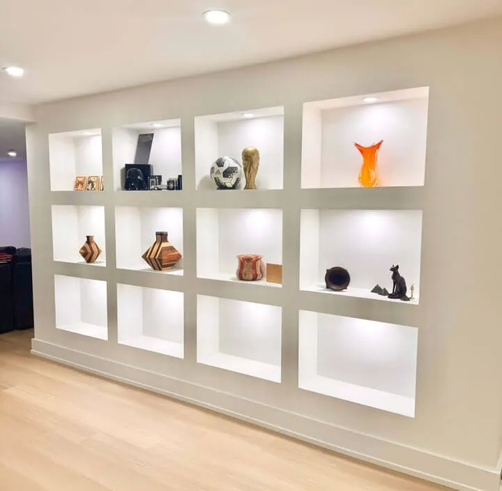 basement renovation feature white wall with lots of Niches holding decorations with custom pot lights in each niche