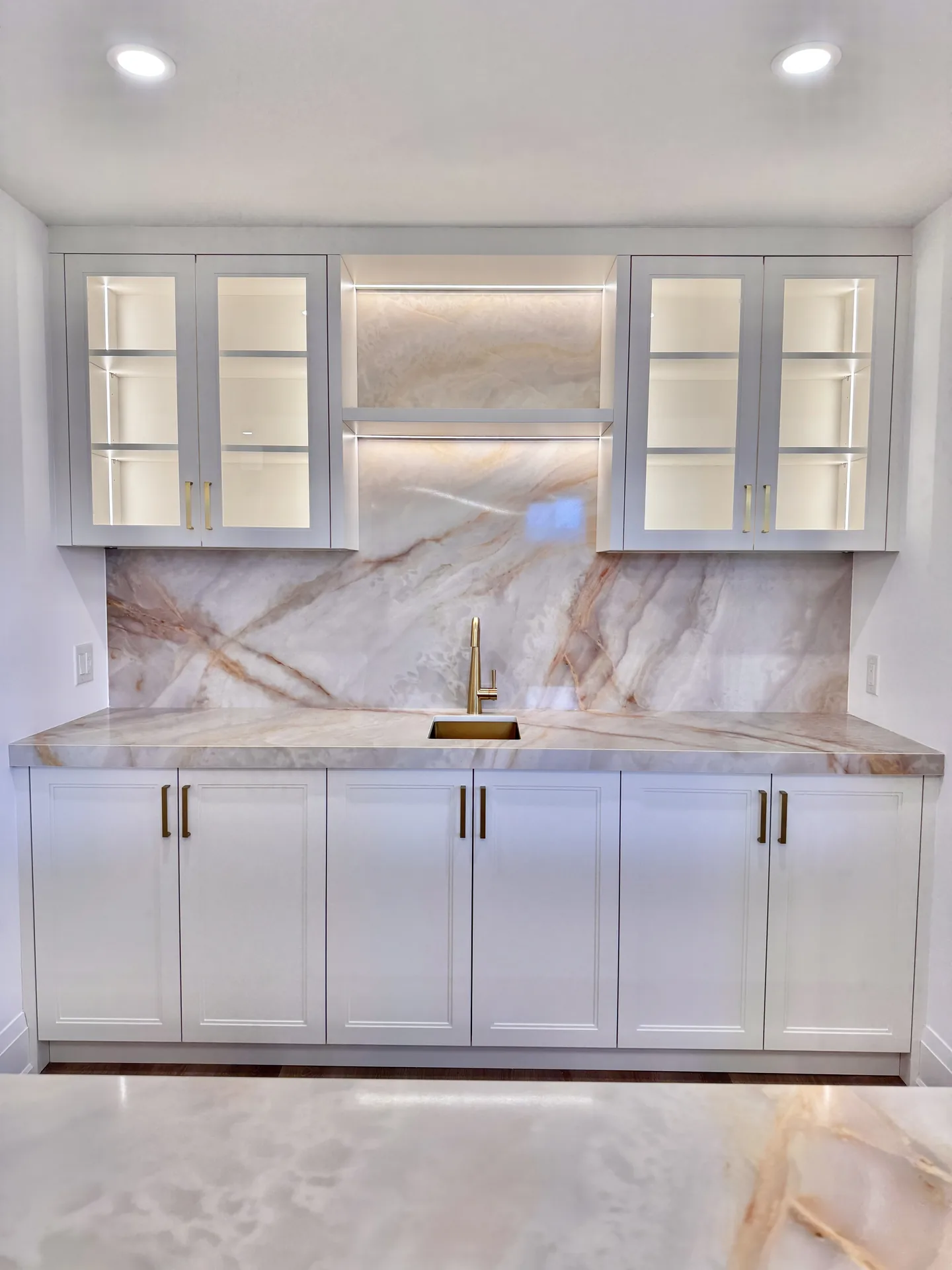 White basement bar with marble backsplash and lit glass cabinets — basement renovation in Woodbridge by Desire Basements