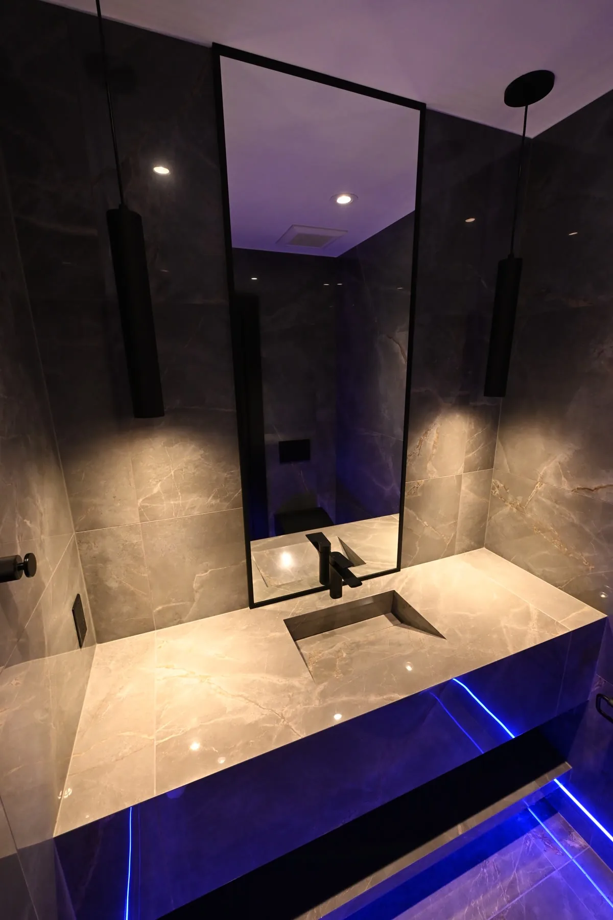 Powder room at Sickick Studio: book-matched grey marble, floating vanity with LED underglow, black-framed mirror and pendant lights