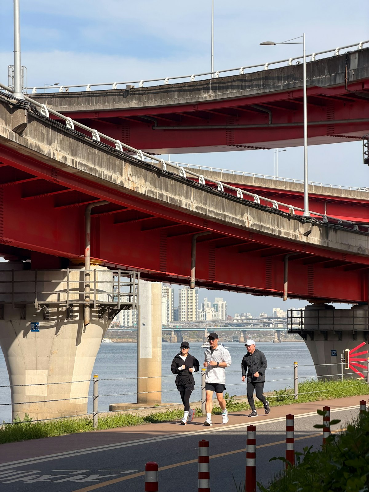 Three people jogging along a city path under bridges
