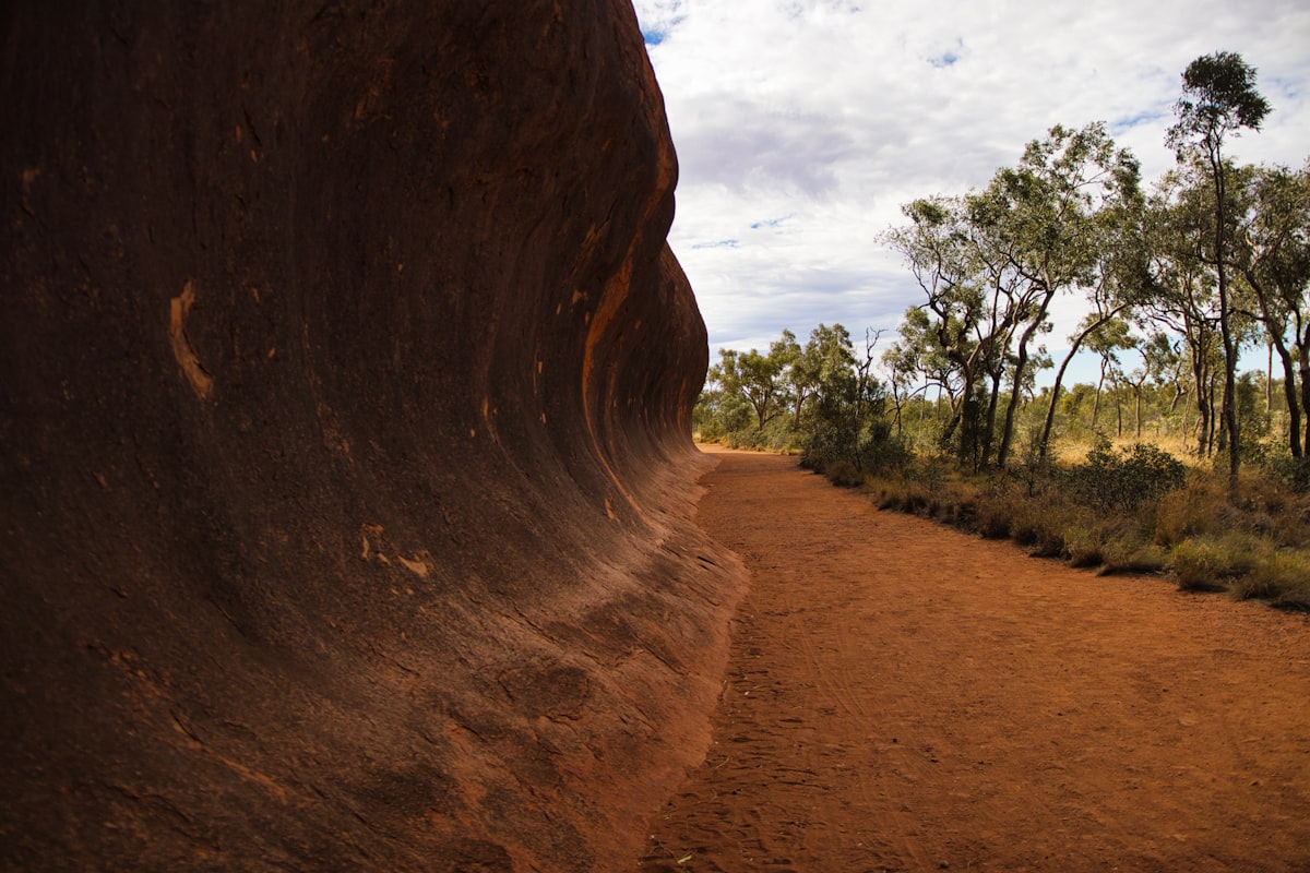 Red dirt path beside large rock formation and trees in the Australian outback