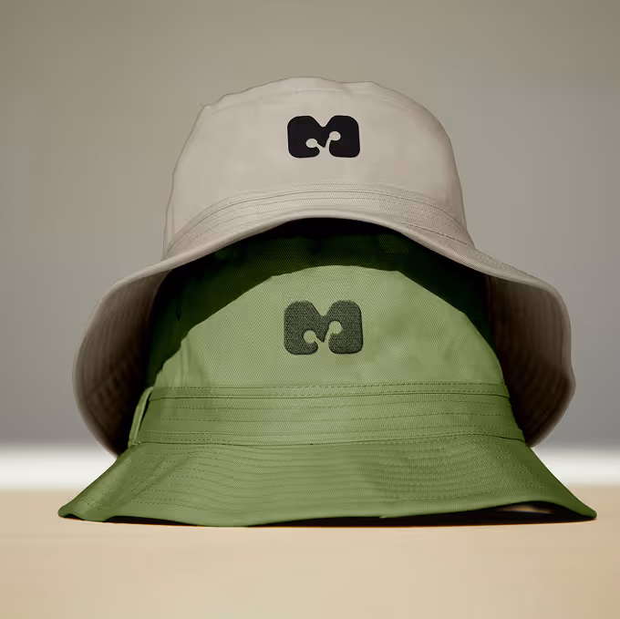 Stack of two bucket hats, one beige over one green, both with a black abstract logo on front. (unblast.com)