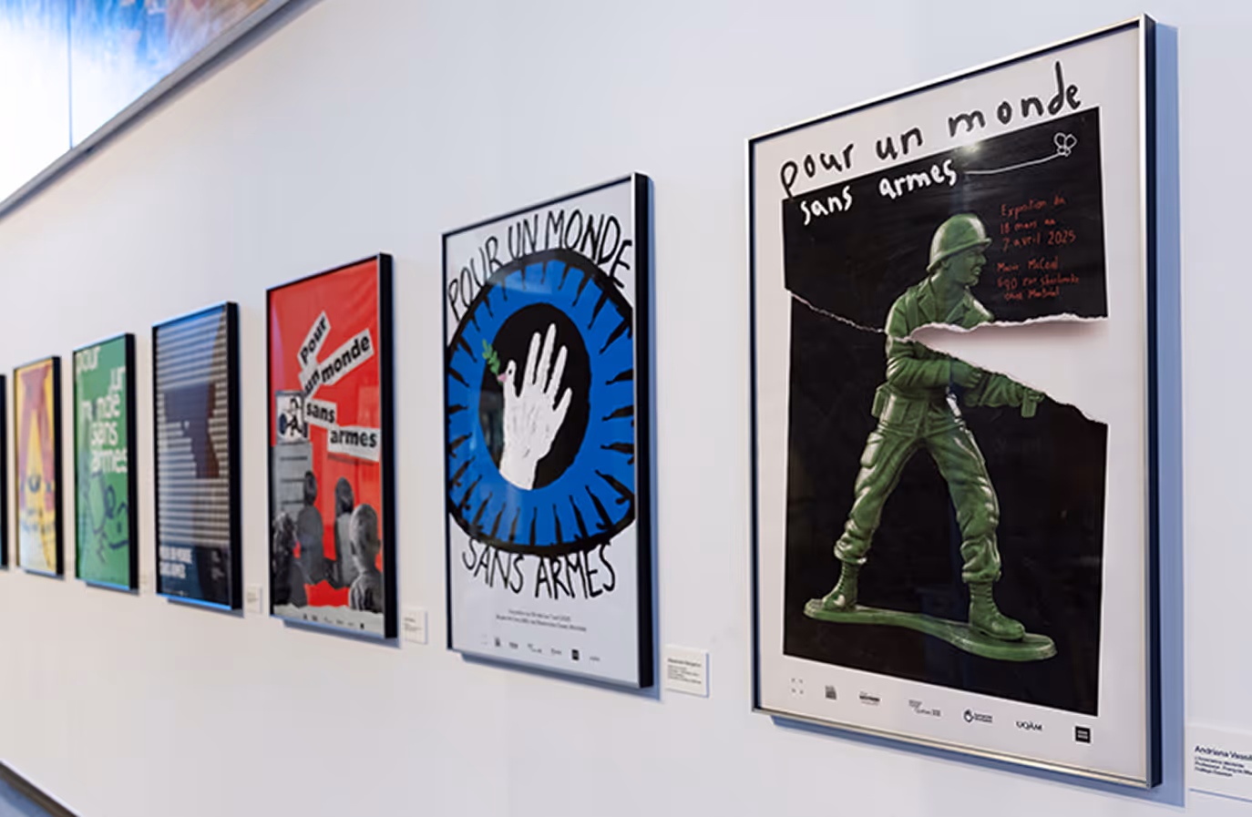 Row of framed posters on a white wall, featuring peace and anti-weapon themes in French. (musee-mccord-stewart.ca)