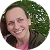 Smiling woman with light brown hair outdoors with green trees in background.