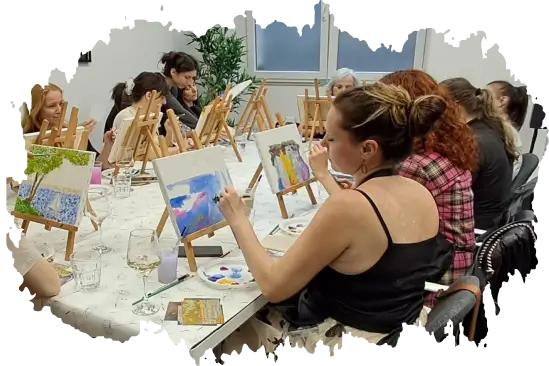 Group of women seated at a table painting on easels during an art class or workshop.