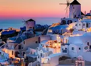 White buildings and windmills on a hillside at sunset with pink and blue sky.
