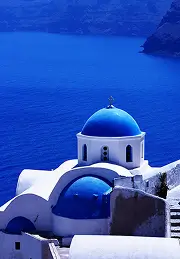 Blue-domed white church overlooking the deep blue sea and rocky cliffs.