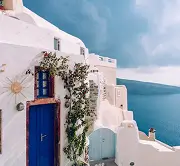 White building with blue door and window overlooking blue sea under cloudy sky.