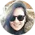 Smiling person wearing sunglasses and a light-colored jacket outdoors.