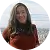 Woman in a rust-colored sweater smiling outdoors with greenery in the background.