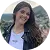 Smiling woman with long dark hair wearing a white T-shirt and a dark jacket outdoors.