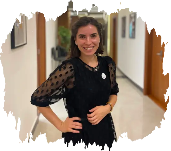 Smiling woman with dark hair in a black dress with sheer sleeves standing in a hallway.