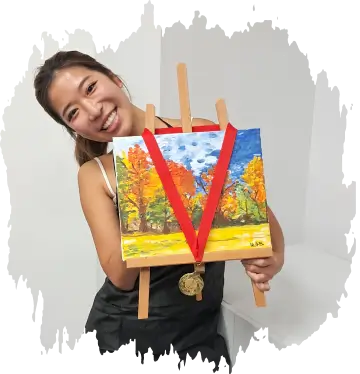 Smiling woman holding a small easel with a colorful autumn landscape painting and a gold medal.