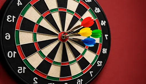 Dartboard with four colorful darts in the bullseye on a red wall.