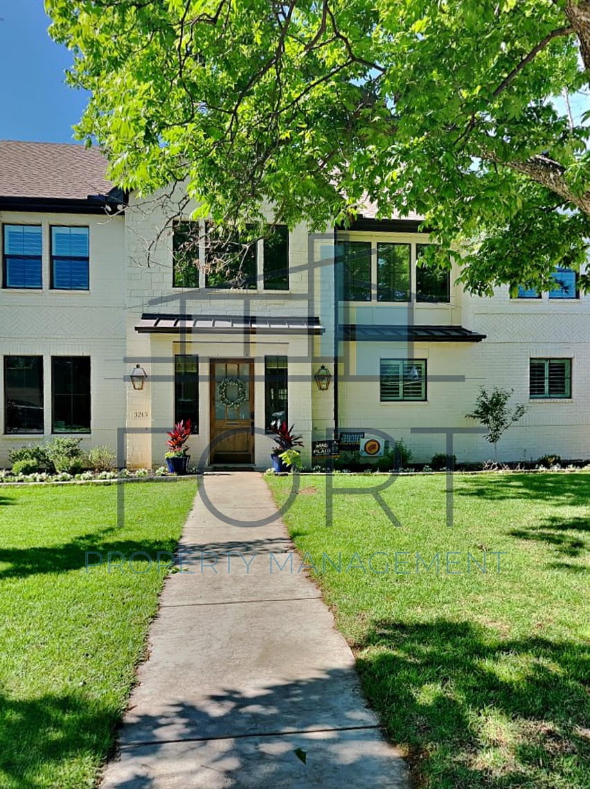 Two-story white brick house with a pathway, green lawn, and tree shadows in front yard.