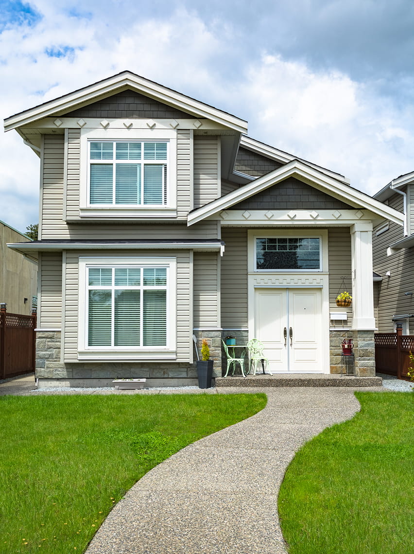 Modern two-story house with gray siding, white trim, large windows, and a curved walkway on green lawn.