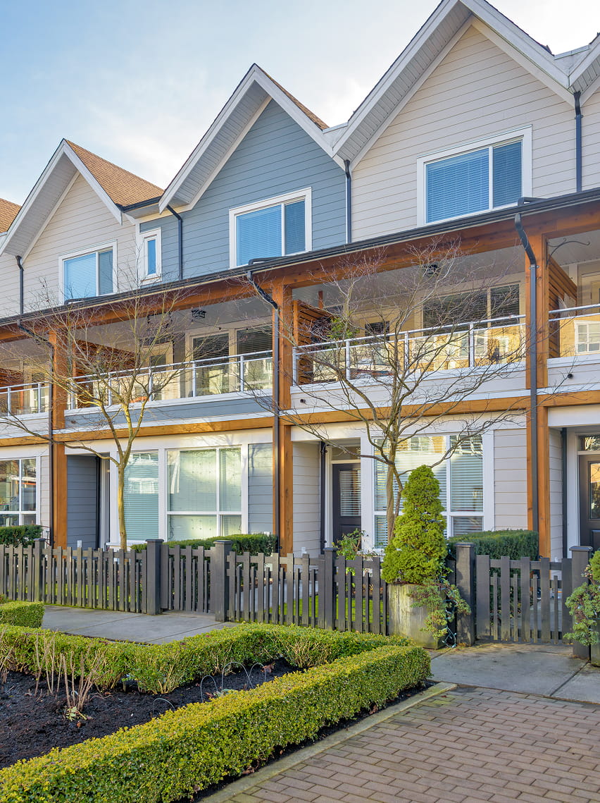 Row of modern townhouses with manicured hedges and bare trees behind a black fence.