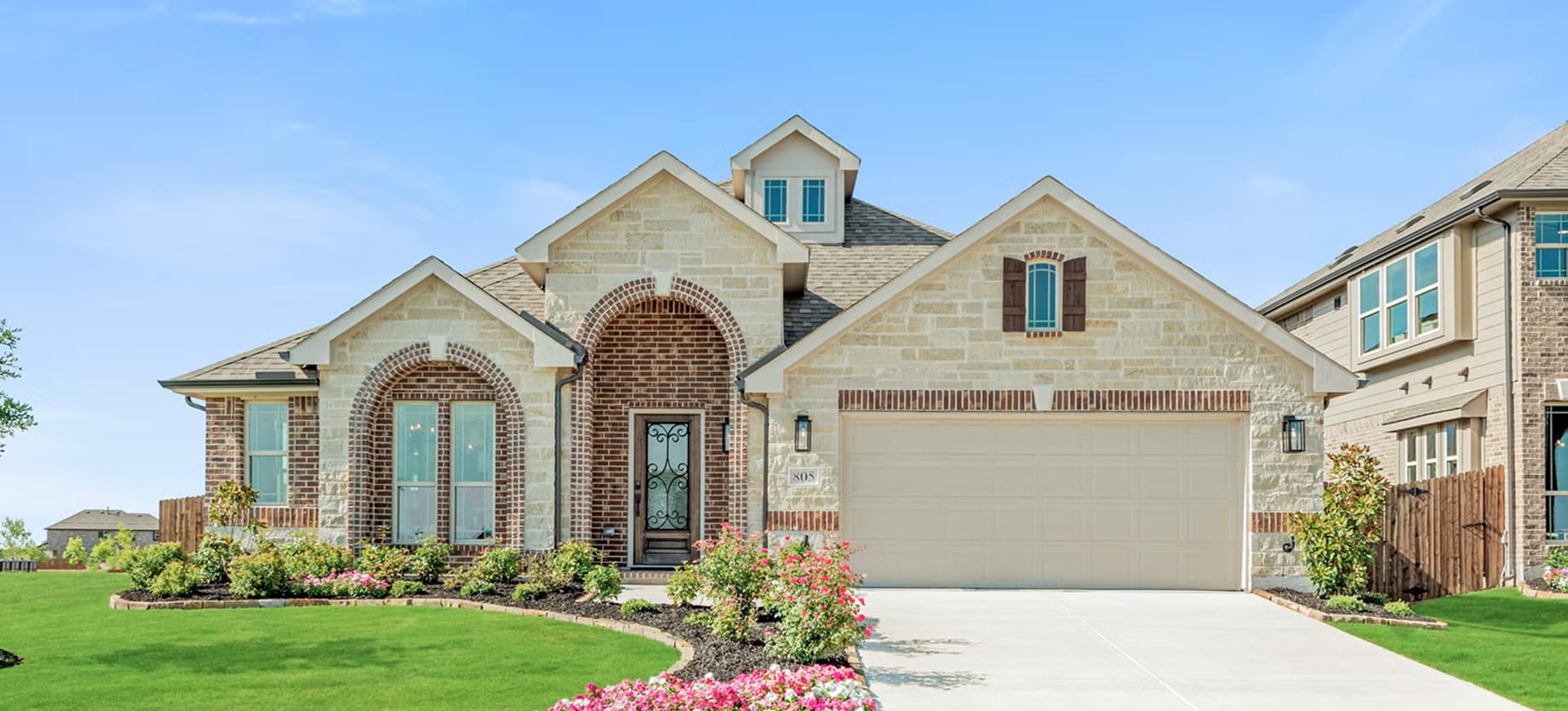 Modern single-story house with light stone and brick façade, arched doorways, garage, and landscaped front yard.