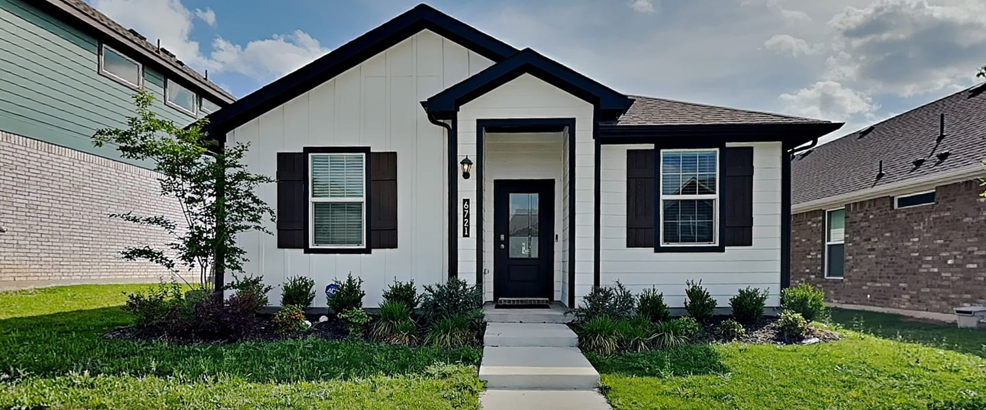 Single-story white house with black trim, black front door, large windows, and shrubs in front yard.