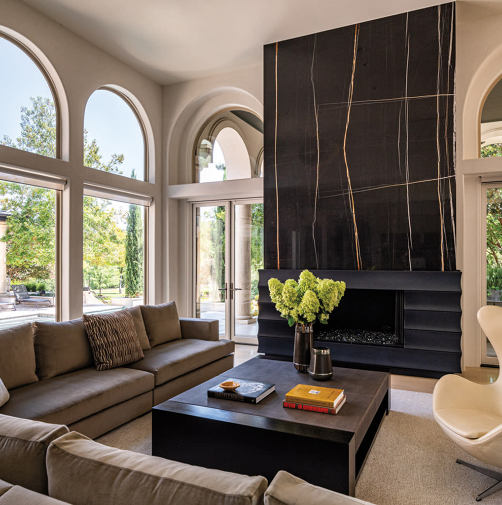 Modern living room with large arched windows, a black marble fireplace, beige sofas, and a coffee table.