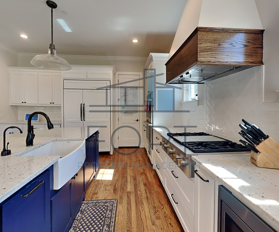 Modern kitchen with white and navy cabinets, farmhouse sink, gas stove, and wooden floor.
