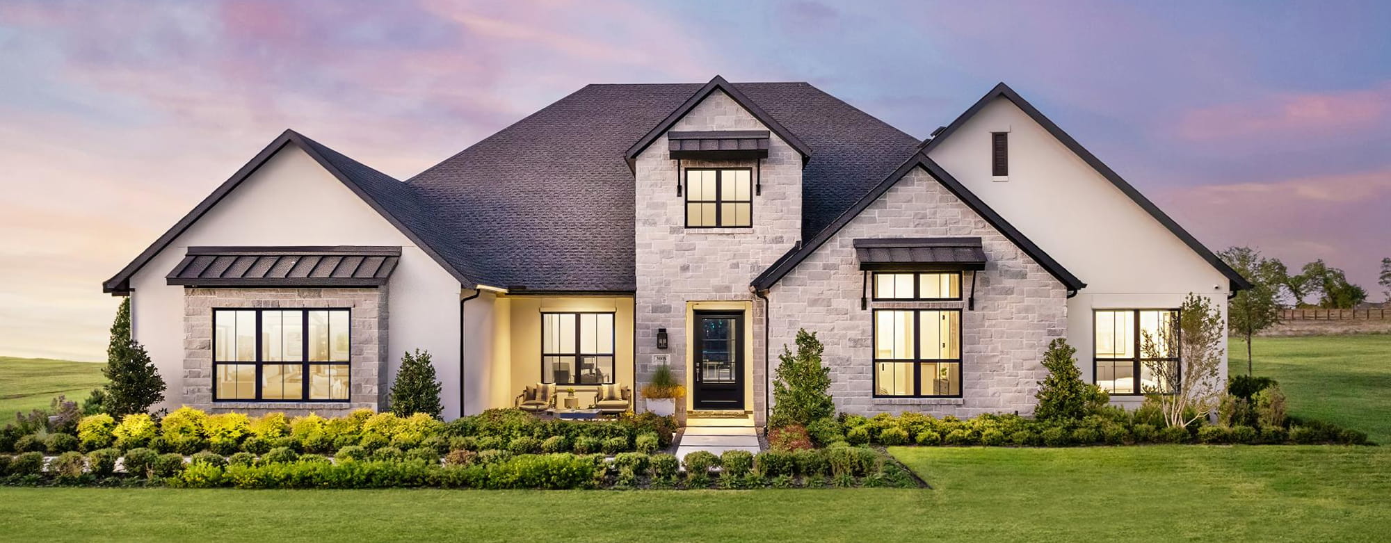 Modern single-story stone and stucco house with dark roof and landscaped front yard at dusk.