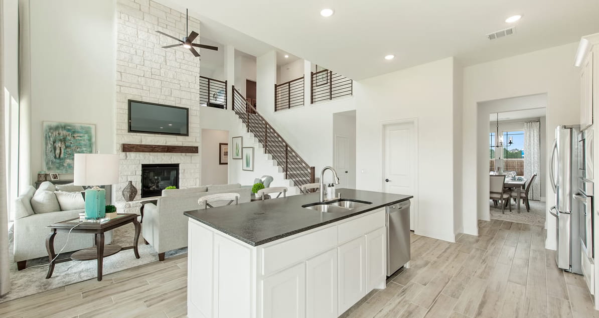 Modern open kitchen and living area with white cabinets, stone fireplace, and staircase with metal railing.