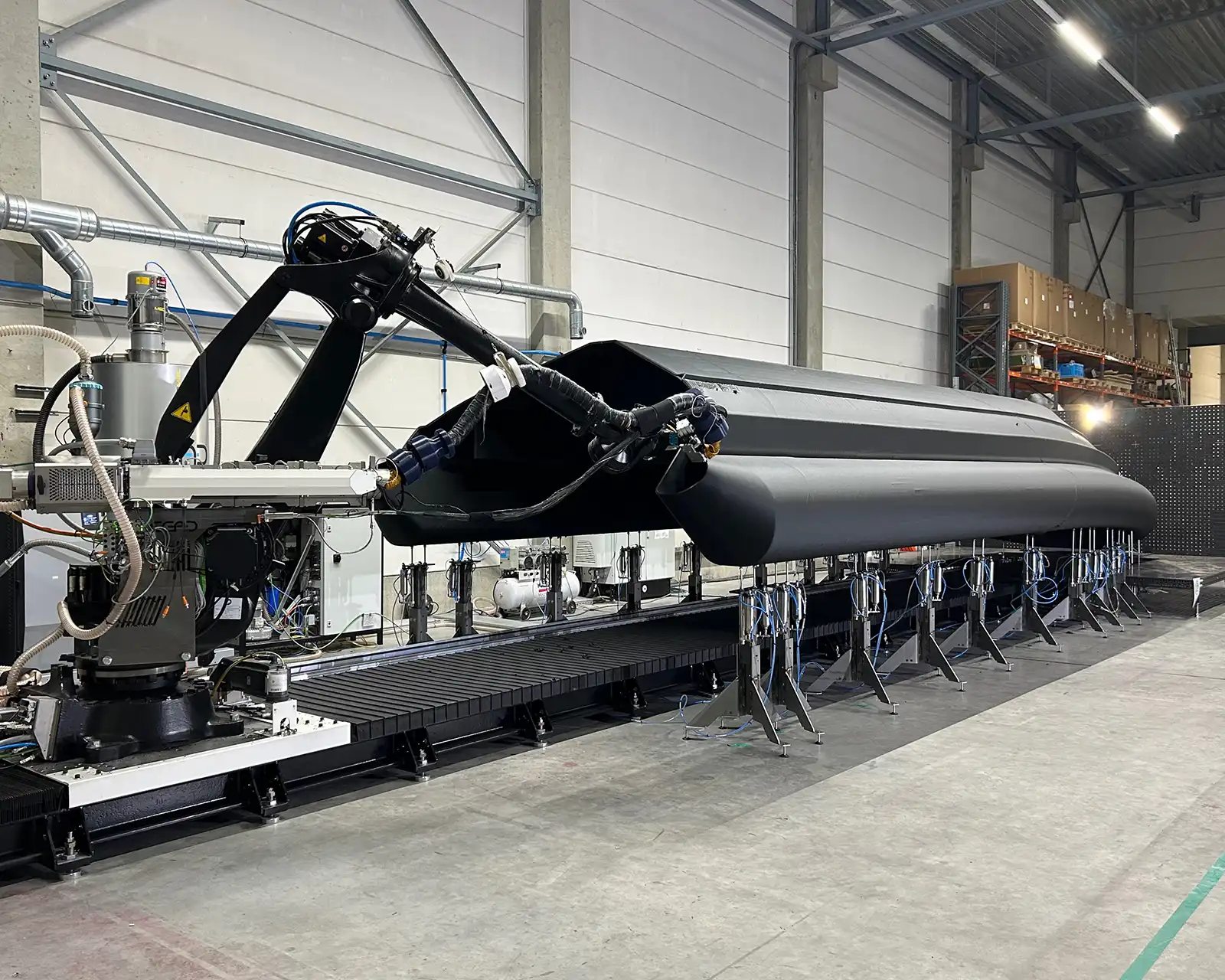 Large-format 3D printer extruding a black HDPro boat hull in the factory