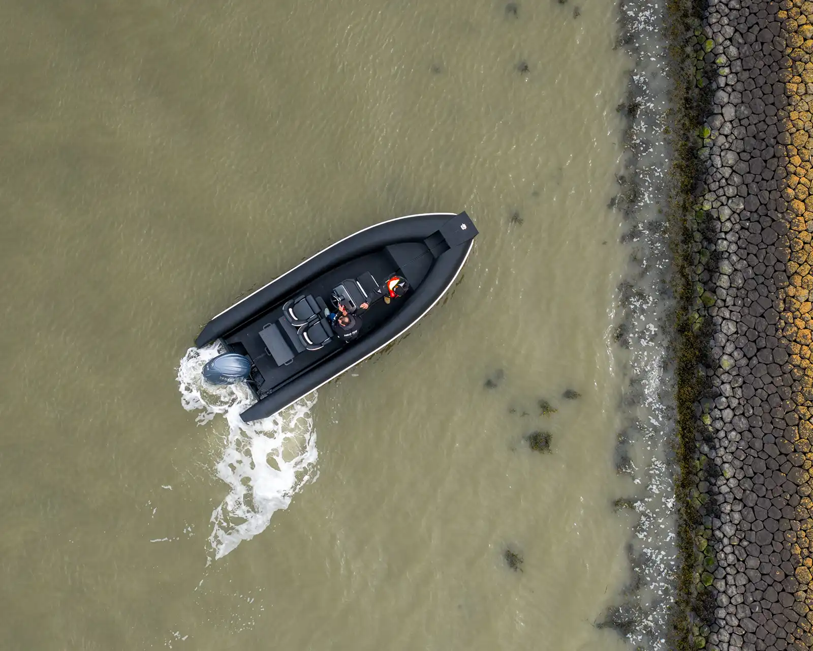 Aerial view of a black HDPro RIB running alongside a stone revetment