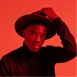 Person wearing a hat and dark clothing with an orange background.